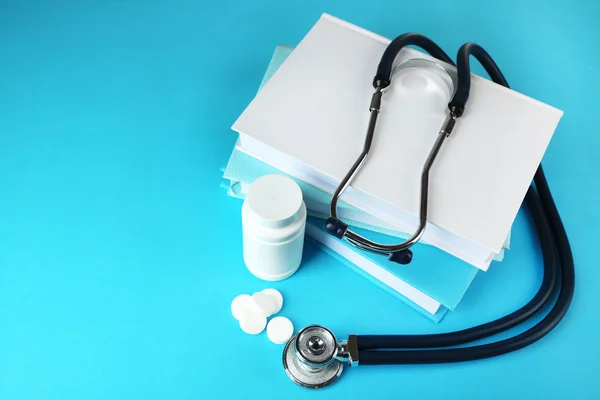 Estetoscopio médico con libros y tabletas sobre fondo azul —  Fotos de Stock