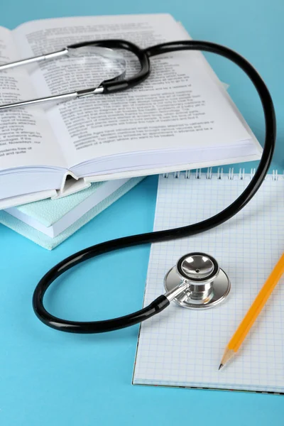 Medical stethoscope with notepad and books on blue background — Stock Photo, Image