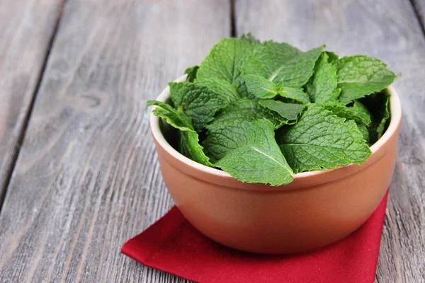 Brown bulat mangkuk daun mint segar di serbet merah di atas meja kayu — Stok Foto