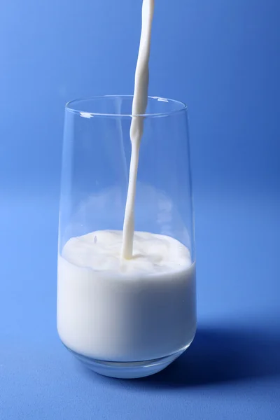 Despeja leite em vidro no fundo azul — Fotografia de Stock