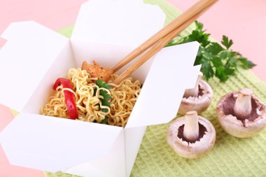Çin eriştesi ve paket servisi olan restoran kutusunda pembe bir arka plan üzerinde yeşil peçete üzerinde sopa