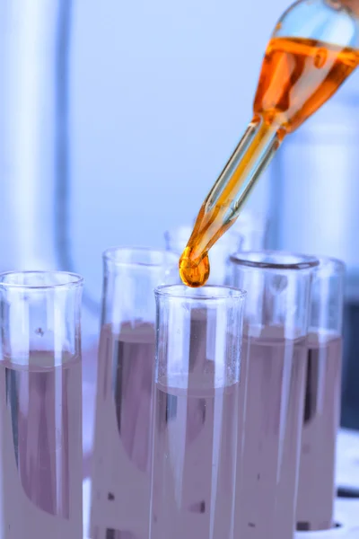 Pipeta de laboratorio con gota de líquido de color sobre tubos de ensayo de vidrio, primer plano —  Fotos de Stock