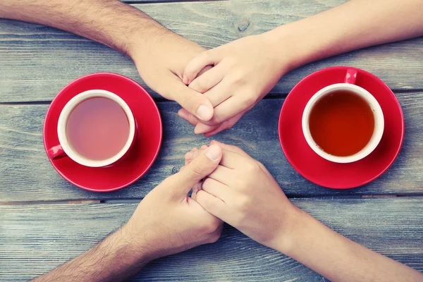 Tea cups and holding hands at the wooden table — Stock Photo, Image