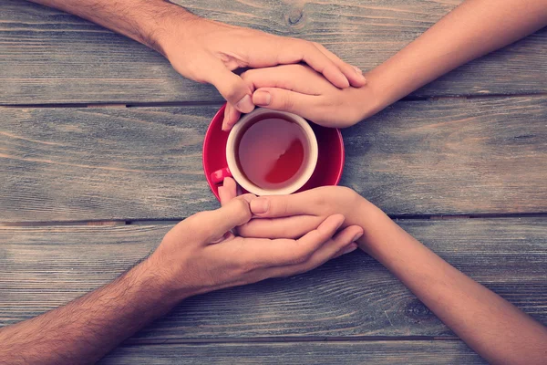 Xícaras de chá e de mãos dadas na mesa de madeira — Fotografia de Stock