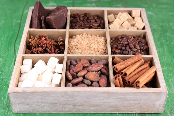 Wooden box with set of coffee and cocoa beans, sugar cubes, dark chocolate, cinnamon and anise over wooden background — Stock Photo, Image