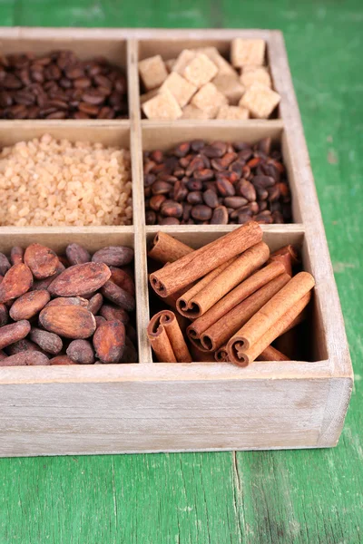 Caja de madera con set de café y granos de cacao, terrones de azúcar, chocolate negro, canela y anís sobre fondo de madera —  Fotos de Stock