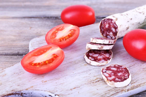 French salami with tomatoes on cutting board on wooden background — Stock Photo, Image