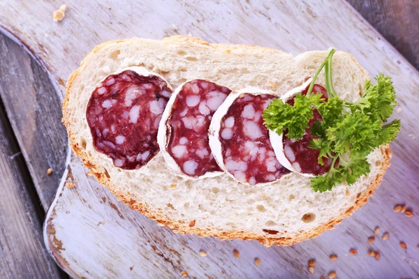 Frans salami met peterselie op sneetje brood op snijplank op houten achtergrond — Stockfoto