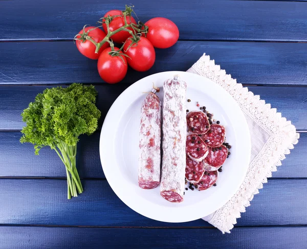 French salami on plate on napkin with parsley and tomatoes on dark blue wooden background — Stock Photo, Image