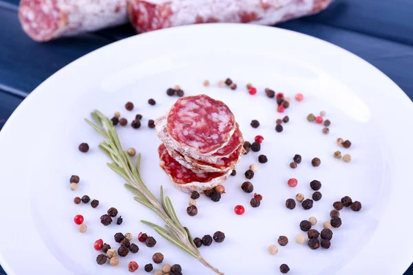 Französische Salami und Pfeffer auf Teller auf dunkelblauem Holzhintergrund — Stockfoto