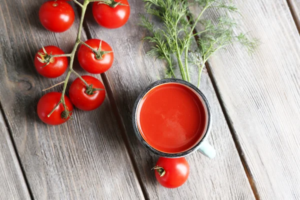 Domácí rajčatové šťávy v barevný hrnek, koření a čerstvá rajčata na dřevěné pozadí — Stock fotografie