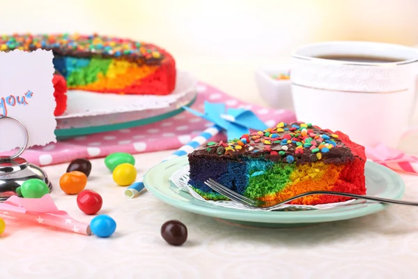 Köstlicher Regenbogenkuchen auf Teller und Tasse mit Kaffee, auf Tisch, auf hellem Hintergrund — Stockfoto