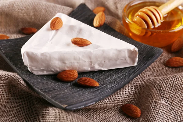 Brie cheese, honey in glass bowl and nuts on sackcloth background — Stock Photo, Image