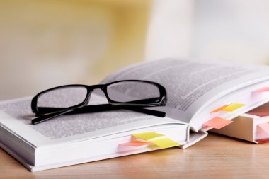 Books with bookmarks and glasses on table on bright background clipart