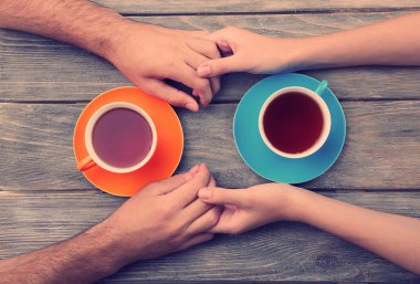 Tea cups and holding hands at the wooden table clipart