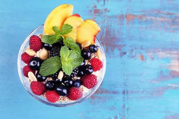 Café da manhã saudável - iogurte com frutas frescas, bagas e muesli servido em tigela de vidro em fundo de madeira colorida — Fotografia de Stock