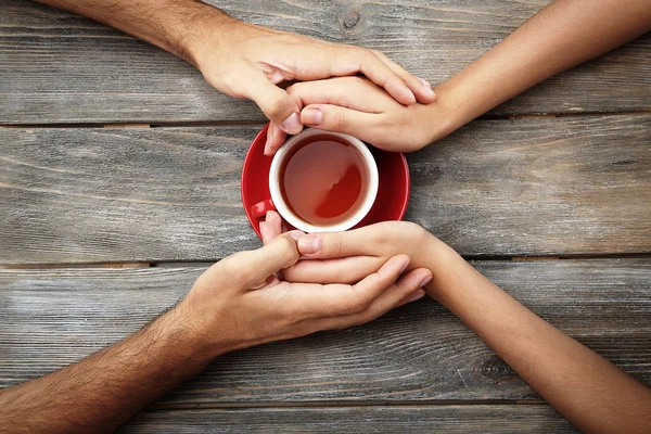 Xícaras de chá e de mãos dadas na mesa de madeira — Fotografia de Stock