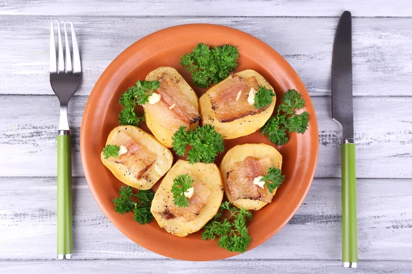 Baked potato with bacon on plate, on wooden background — Stock Photo, Image