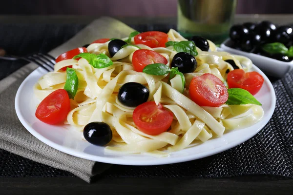 Espaguetis con tomates, aceitunas y hojas de albahaca en primer plano — Foto de Stock