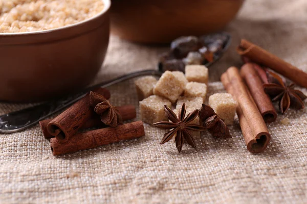 Brown sugar cubes and crystal sugar, spices in bowl on sackcloth background — Stock Photo, Image