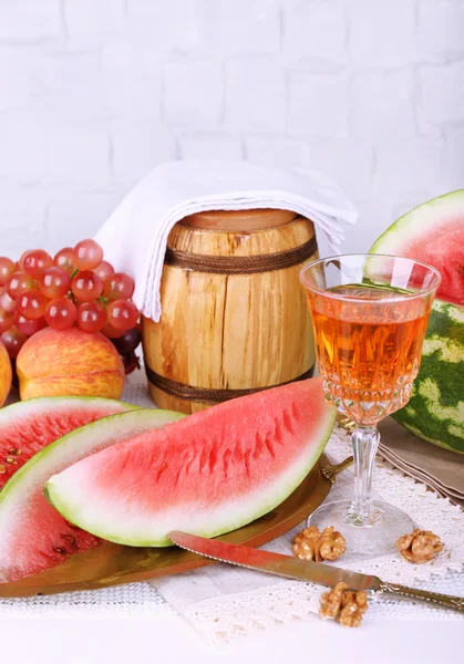 Skład dojrzały arbuz, owoce, wino różowe w szklane i drewniane beczki na drewnianej tablicy kolorów, na jasnym tle — Zdjęcie stockowe