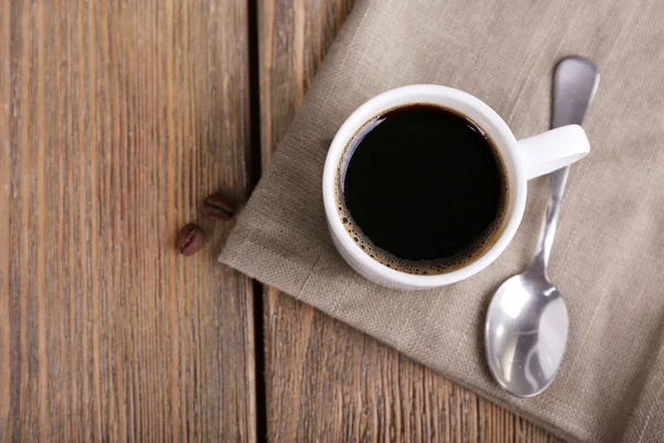 Xícara de café e grãos de café em guardanapo em fundo de madeira — Fotografia de Stock