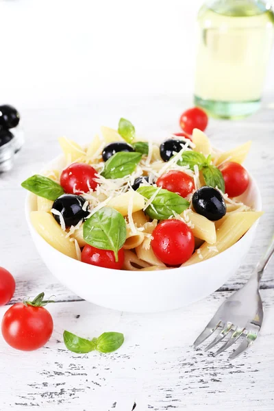 Pasta with tomatoes, olives and basil leaves in bowl on wooden table on natural background — Stock Photo, Image