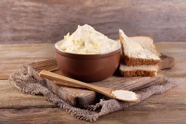 Verse zelfgemaakte boter in kom en gesneden brood, op houten achtergrond — Stockfoto