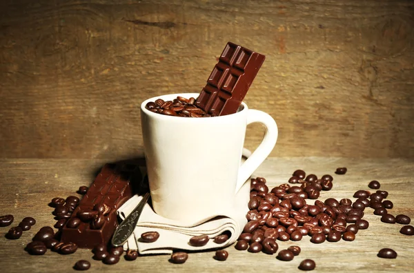 Cup with coffee beans and dark chocolate glaze on wooden background — Stock Photo, Image