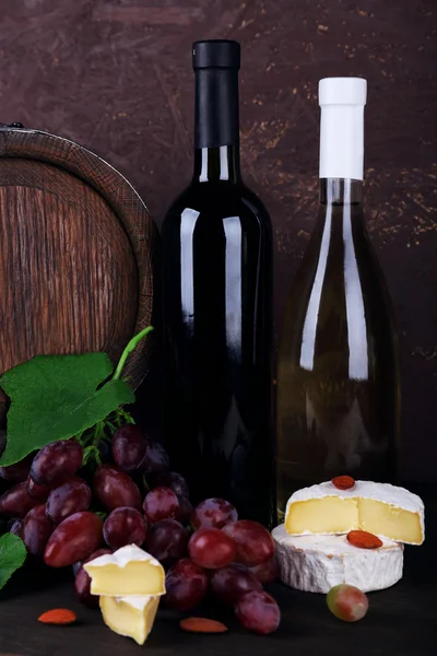 Vino en botellas, Camembert y queso brie, uvas y barril de madera sobre mesa de madera sobre fondo de madera — Foto de Stock