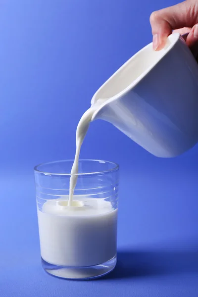 Pours milk in glass on blue background — Stock Photo, Image