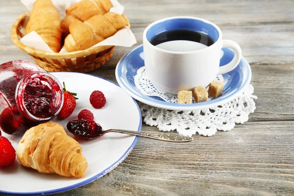 Breakfast with tea, raspberry jam and fresh croissants on wooden background