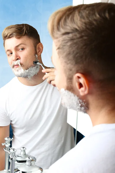 Jeune homme rasant sa barbe dans la salle de bain — Photo