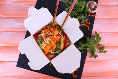 Çin eriştesi ve paket servisi olan restoran kutusunda pembe bir arka plan üzerinde siyah mat sopa