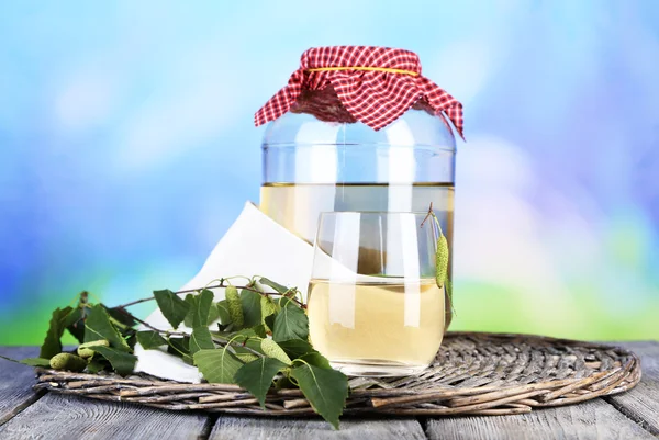 Flagon of birch juice on wicker round mat on wooden table on nature background — Stock Photo, Image