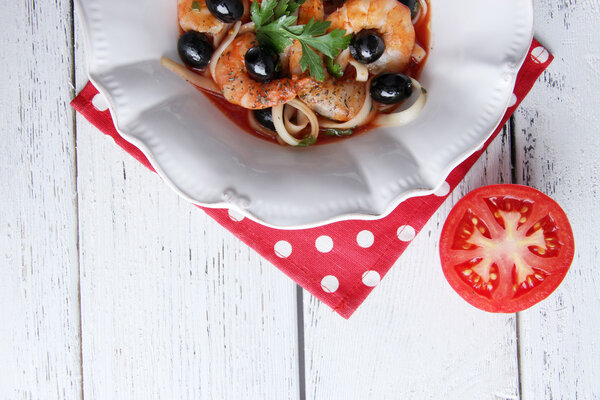 Fresh prawns with spaghetti, olives and parsley in tomato sauce in a round white plate on a napkin on white wooden background