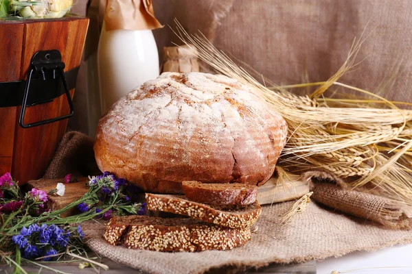 Cesta de madera grande, orejas de pan, flores secas y leche sobre fondo saqueador — Foto de Stock