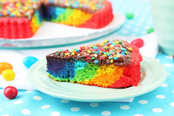 Delicioso pastel de arco iris en el plato, sobre fondo de mantel —  Fotos de Stock