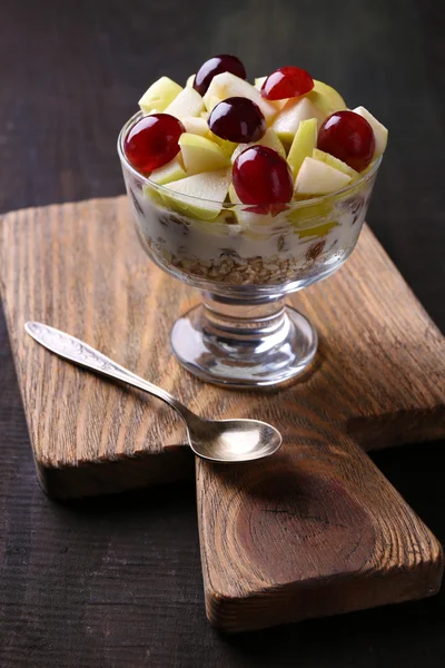 Gezond ontbijt - yoghurt met vers druif en apple segmenten en muesli geserveerd in glazen kom, op houten achtergrond — Stockfoto