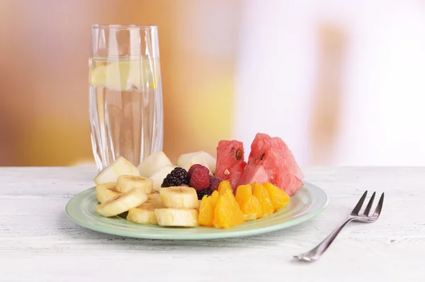 Rebanadas de frutas y bayas en el plato con un vaso de agua en la mesa sobre fondo de madera —  Fotos de Stock