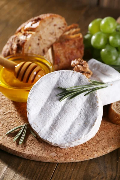 Camembert cheese, bread, honey and grapes on cutting board on wooden background — Stock Photo, Image