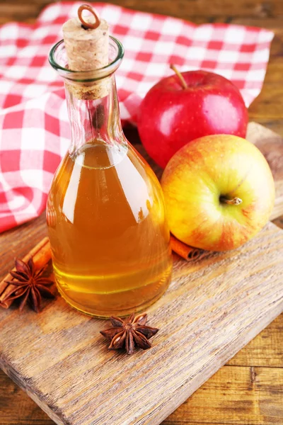 Sidro di mele in bottiglia di vetro con bastoncini di cannella e mele fresche sul tagliere, su fondo di legno — Foto Stock