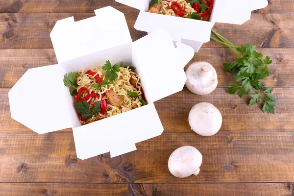 Chinese noodles in takeaway boxes with mushrooms and parsley on wooden background — Stock Photo, Image