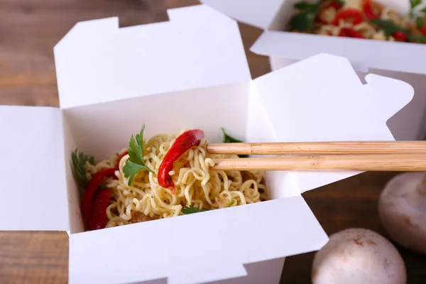 Chinese noodles in takeaway boxes with mushrooms and parsley on wooden background — Stock Photo, Image