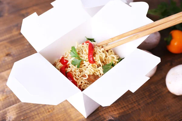 Chinese noodles in takeaway boxes with mushrooms and parsley on wooden background