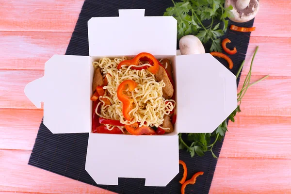 Chinese noodles in takeaway box on black mat on pink background — Stock Photo, Image