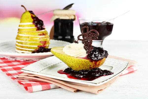 Tasty dessert with pear, cream and berry sauce on plate, on color wooden table, on bright background — Stock Photo, Image