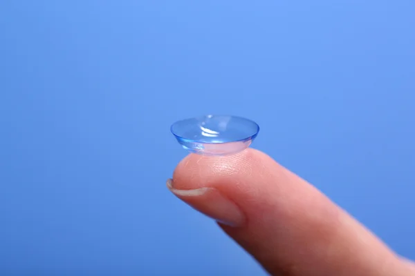 Contact lens op vinger op blauwe achtergrond — Stockfoto