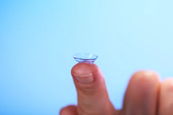 Contact lens on finger on blue background — Stock Photo, Image