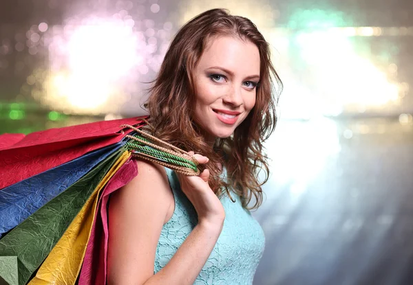 Beautiful young woman with shopping bags on bright background — Stock Photo, Image